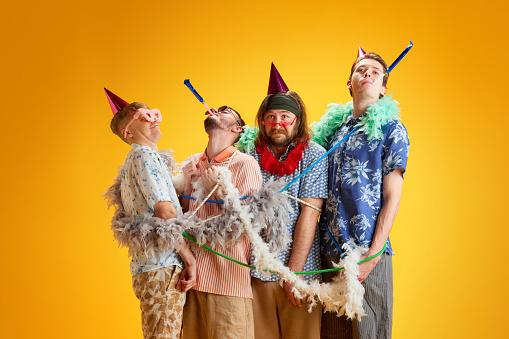 Birthday party. Friends, stylish emotion men tied with decorations, celebrating against yellow background. Concept of leisure, vacation, emotions, friendship, fun, bachelor party