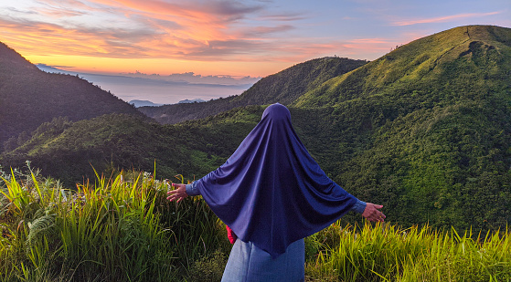 A woman wearing hijab take photo with the Mongkrang hill in the background at dawn,location in Wonogiri,Indonesia.