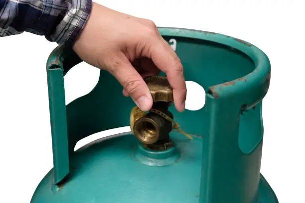 Photo of Male hand is closing the valve of lpg gas tank for safety. Files can use clipping parts.