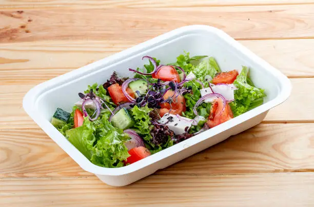 Photo of Greek salad with feta cheese. Healthy diet.Takeaway food. On a wooden background.