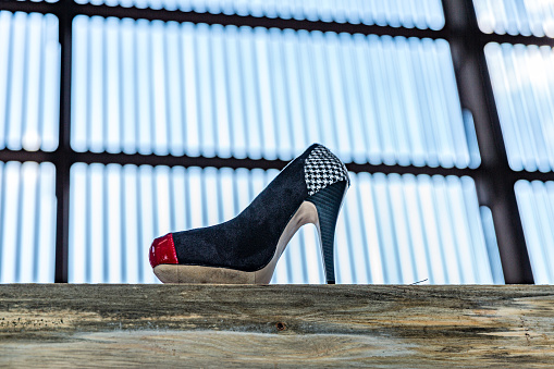 High-heeled women shoe on wooden plank against huge window with blue light in blurred background, black, red and white color combination. Beauty, glamor and fashion concept