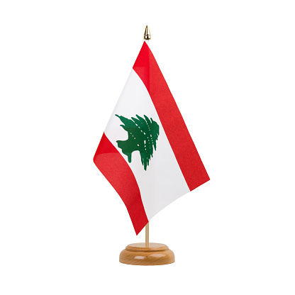 A beautiful miniature Lebanon desk flag isolated on a white background. The little pennant is elegantly attached to a small wooden flag stand.