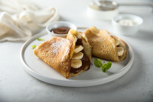 Person eating crepes with filling. Tasty breakfast on gray background.