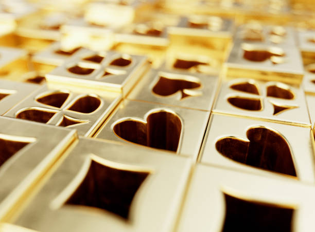 An extruded  array of gold casino card heart, diamond, spade, and club symbols on a flat surface - 3D render