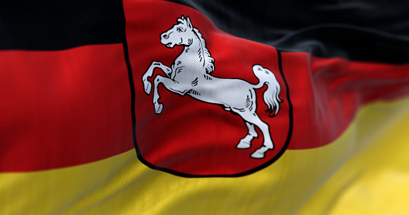 Close-up of Lower Saxony state flag waving. Black, red and yellow stripes with coat of arms in the center. German state. 3d illustration render. Selective focus. Rippling fabric. Textured background