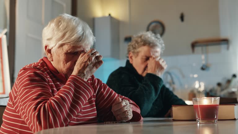 SLO MO Elderly Women Praying with Eyes Closed and Hands Clasped Sitting at Table with Holy Bible at Home