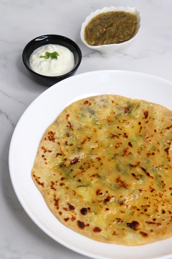 Indian Food. Aloo Paratha or Indian Potato stuffed Flatbread. Served with butter, ghee, yogurt or curd and roasted tomato chutney. over light background with copy space.