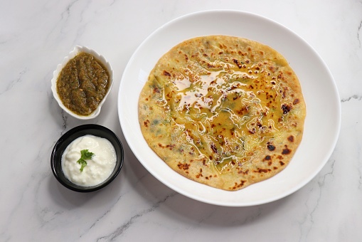 Indian Food. Aloo Paratha or Indian Potato stuffed Flatbread. Served with butter, ghee, yogurt or curd and roasted tomato chutney. over light background with copy space.
