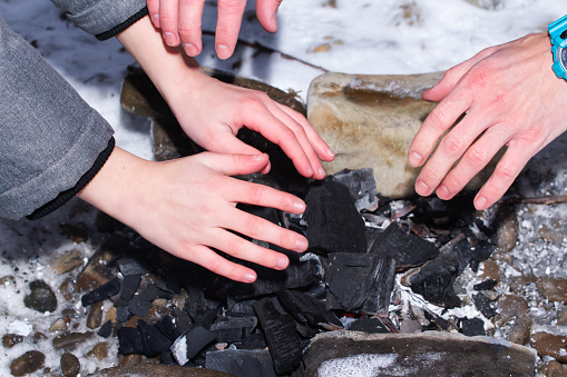 Мальчик с папой греют руки у горящих углей зимой. Семейный отдых.