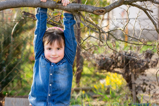 A little girl climbs a tree in the yard during a spring day.