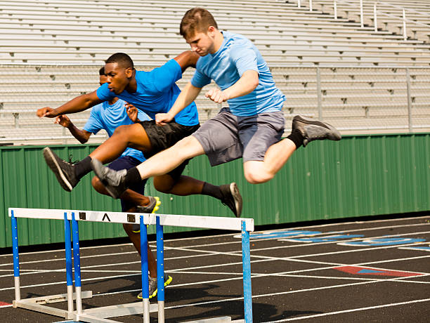 Sports: Three high school boys run a hurdles race. Three high school boys running a hurdles track event.  Selective focus on hurdles, runners are in motion.  hurdling track event stock pictures, royalty-free photos & images