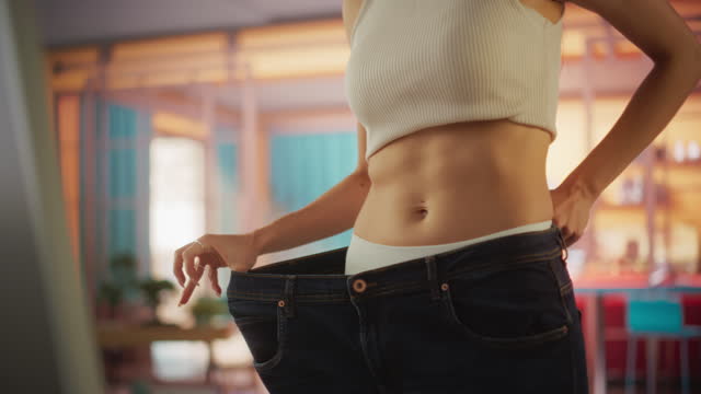 Close Up Slow Motion on the Waste of Beautiful Fit Woman Trying on her Old Jeans Before Diet. Female Noticing Difference Made by a Healthy Lifestyle. Results of Healthy Eating and Working Out