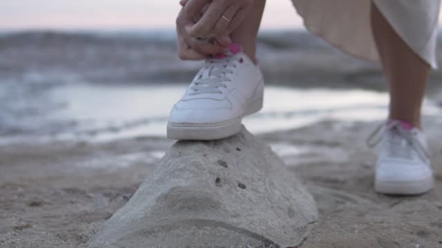 Close-up, a woman tying a shoelace on her sneakers on a stone by the sea