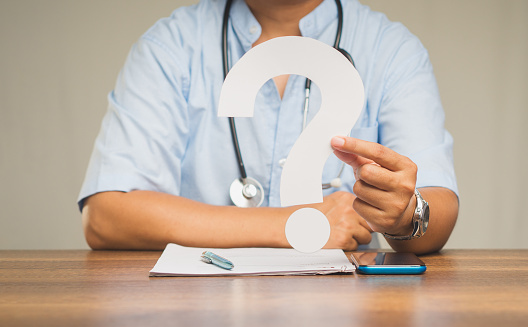 Close-up of hand doctor holding a white question mark while sitting at the table in the hospital. Concept of Medicine and Healthcare