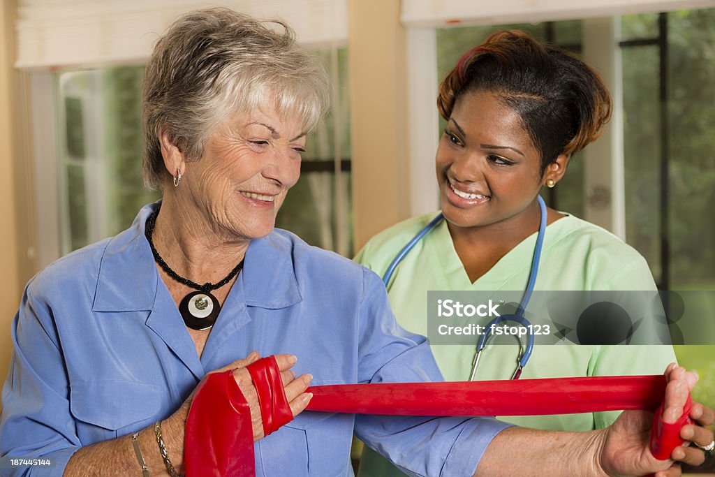 Medical:  Home healthcare nurse helps woman with band therapy. Senior woman does resistance band exercises with her physical therapist. 20-29 Years Stock Photo