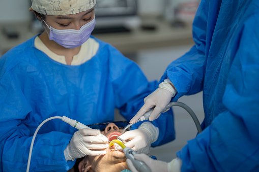 Female dentist in face mask and glasses doing treatment for patient blonde lady, holding dental tools, wearing rubber gloves. Stomatology, dentistry, modern dental clinic concept