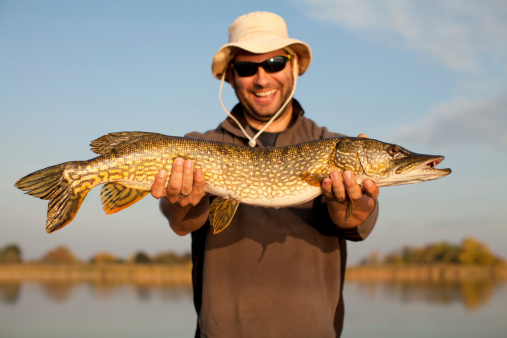 Excited fisherman with big pike posing with the lake in the background