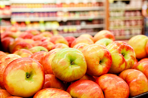 Fresh apples stacked on shelf of grocery store or fresh food market.  Shelves of groceries in background. 