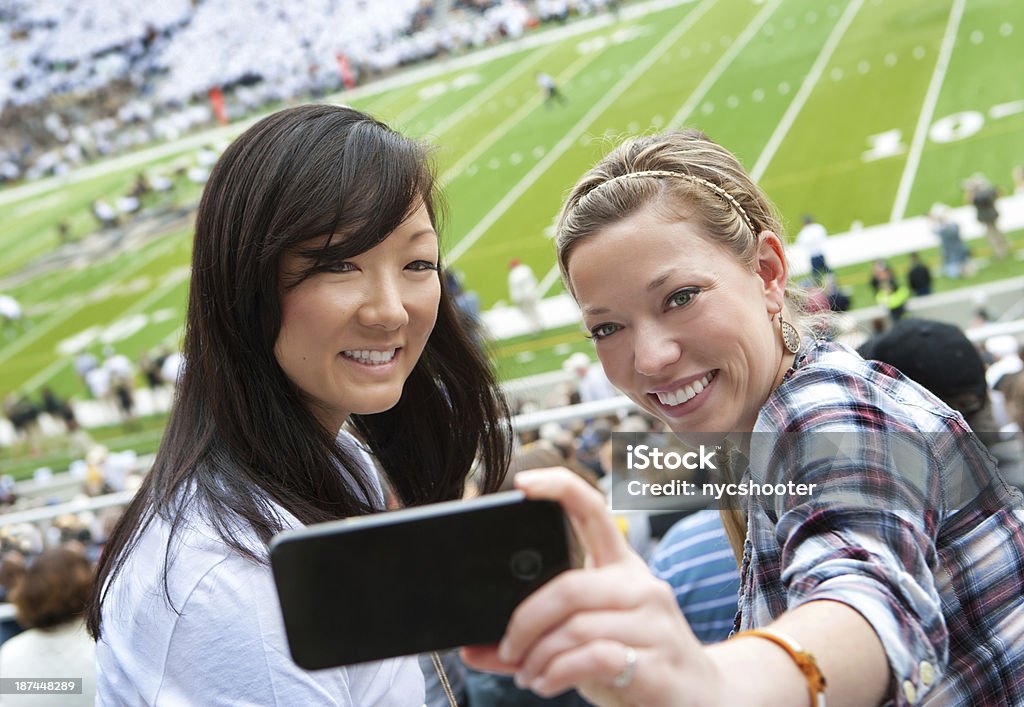 Taking a picture at sporting event Young Asian woman spectator taking a picture at sports event with her smart phone. American Football - Sport Stock Photo