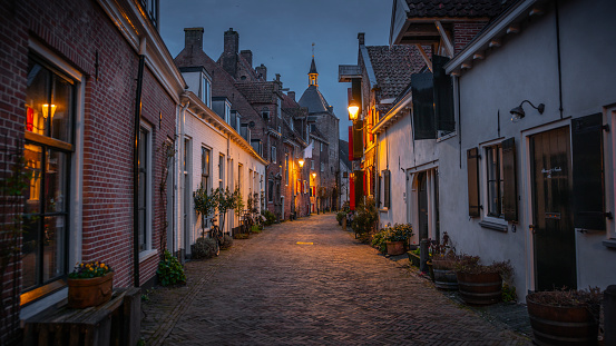 Empty cobblestone city street, surrounded by historic medieval buildings in the old town of Amersfoort. Illuminated street lights at dawn. Holland in the Netherlands, Europe.