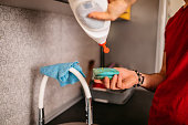 Young Man Putting Soap Sud On The Sponge Above The Kitchen Sink At Home