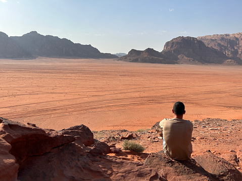 Young man sitting and observing the sunset in the desert of Wadi Rum, Jordan. Young boy on her back enjoying the solitude of the desert at sunset