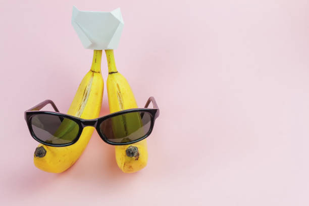 two torn bananas with a hat and sunglasses on a pink background with space for text