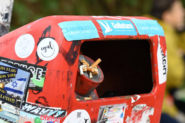 In the cropped image, a woman's hand is shown throwing crumpled paper into a trash bin.