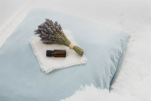 Using lavender flower essential oil for better good night sleep. Calming relaxing aromatherapy concept. Lavender oil and bouquet of lavender flowers on soft pillow in home bedroom. Minimal white.