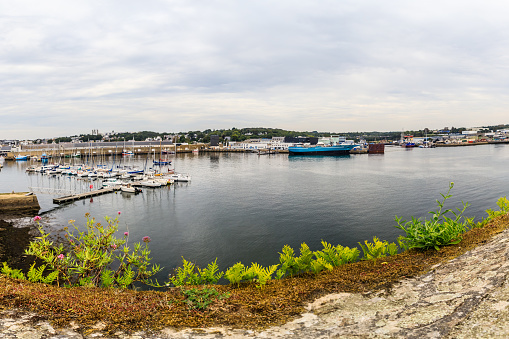 Captured in this panoramic photograph is the breathtaking vista from the medieval fortress on the port island of Concarneau. Perched atop the ancient stone walls, the vantage point provides an expansive view of the bustling harbor below, creating a mesmerizing panorama that unfolds the maritime story of this coastal enclave.\n\nTo the right, historic sailboats and modern vessels peacefully coexist in the harbor, their masts reaching toward the sky. The quayside, lined with colorful facades and waterfront cafes, adds a vibrant touch to the scene. As the panorama extends to the left, the tranquil waters of the harbor glisten under the sunlight, offering a serene contrast to the lively maritime activity.\n\nFrom this elevated perspective, the fortified walls of the medieval fortress frame the view, adding a sense of historical grandeur to the coastal landscape. The distant horizon merges seamlessly with the azure sky, enhancing the sense of openness and serenity that envelops the panoramic tableau.\n\nThis image captures the essence of Concarneau's island fortress, where the convergence of history, maritime culture, and natural beauty unfolds in a spectacular panoramic tapestry, inviting viewers to immerse themselves in the timeless charm of this coastal haven.