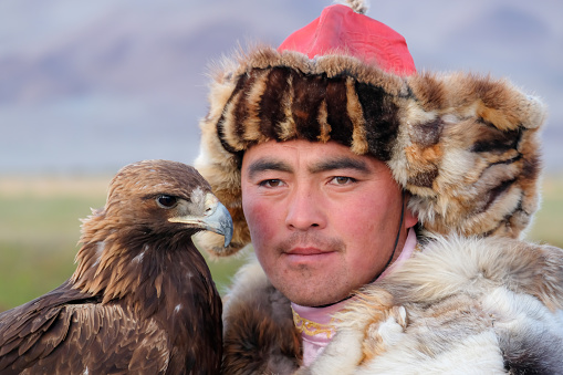 A Kazakh eagle hunter, holding his Golden Eagle up to his face at the Sagsai Golden Eagle Festival held on 17th-18th September 2023, near the small town of Sagsai, in the Bayan-Ulgii province of Western Mongolia. Set in the Altai Mountain range, the nomadic eagle hunters, dressed in traditional fur and embroidered clothing, gather to compete with their eagles, in various competitions that show the skill and bond between the hunter and their eagle.