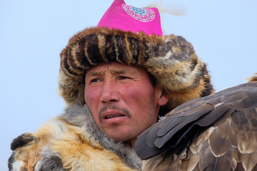 A Kazakh eagle hunter, wearing a traditional fur and embroidered hat, holding his Golden Eagle at the Sagsai Golden Eagle Festival held on 17th-18th September 2023, near the small town of Sagsai, in the Bayan-Ulgii province of Western Mongolia. Set in the Altai Mountain range, the nomadic eagle hunters, gather to compete with their eagles, in various competitions that show the skill and bond between the hunter and their eagle.