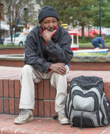 Homeless african american man sitting outdoors with backpack.