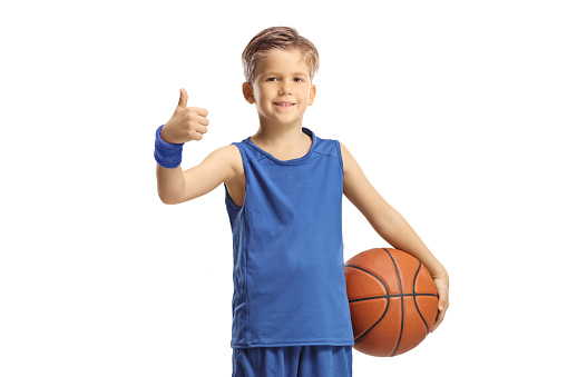 Boy in a blue jersey holding a basketball and showing thumbs up isolated on white background
