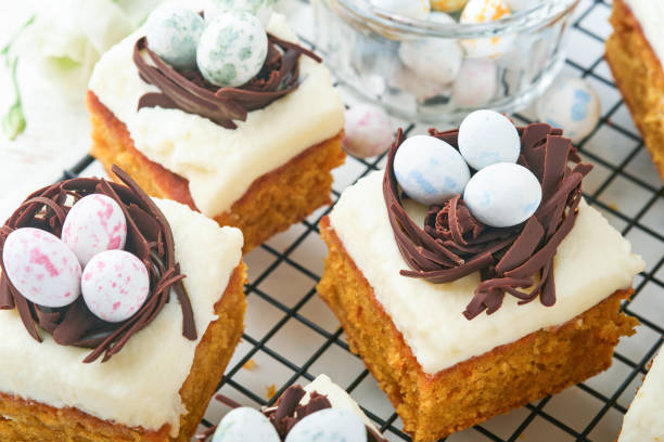 istock Easter carrot cake bars decorated with chocolate nest and chocolate candy eggs blossoming cherry or apple flowers on rustic light wooden backgrounds. Easter holiday meal. Traditional Easter food. 1874627255