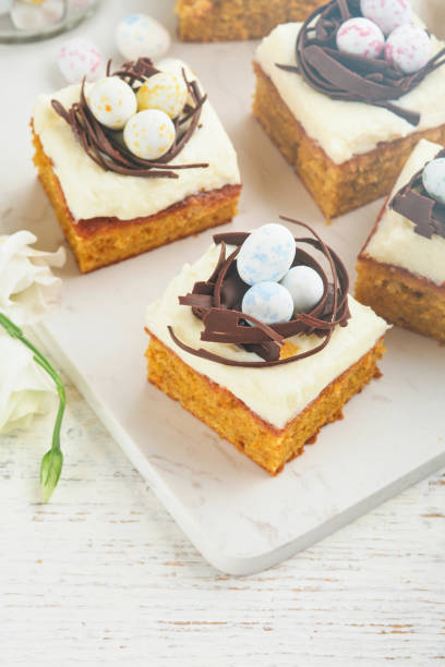 istock Easter carrot cake bars decorated with chocolate nest and chocolate candy eggs blossoming cherry or apple flowers on rustic light wooden backgrounds. Easter holiday meal. Traditional Easter food. 1874627823