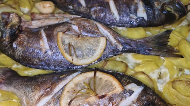 Sea Bream fish baked in a tray among potatoes with garlic lemon and rosemary. Tasty gilthead seafood, fresh cooked with hot steam coming out of meal