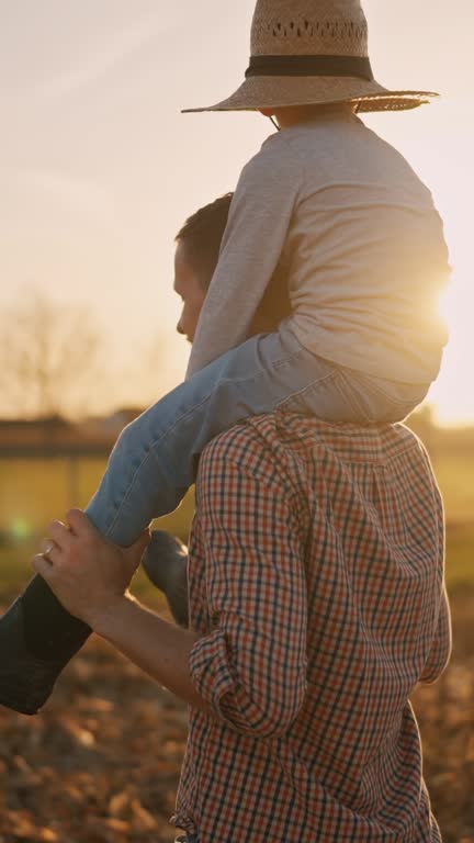 SLO MO Farmer Carrying Son on his Shoulders while Walking on Stubble Corn Field under Clear Sky at Sunset