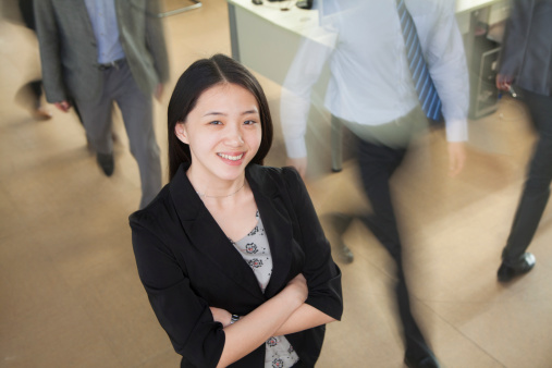 Young businesswoman smiling in the office, businessmen walking all around her