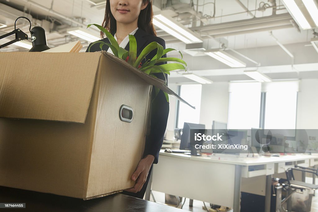 Young businesswoman carrying a box in an office Young businesswoman moving box with office supplies Moving Office Stock Photo