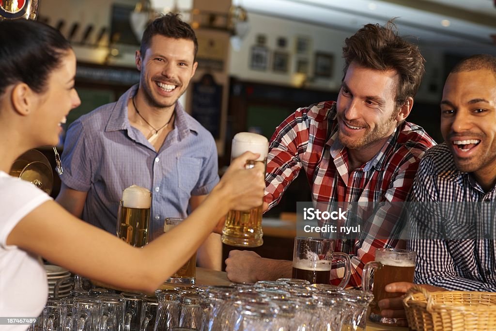 Friends drinking beer at counter in pub Happy friends drinking beer at counter in pub, chatting with female bartender, smiling.. 20-29 Years Stock Photo