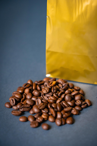 Mock-up golden metallic paper pouch bag on a blue background lying at coffee beans with cinnamon