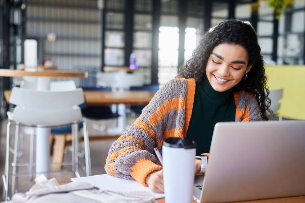 istock Smiling female college student doing homework in a school cafeteria 1874693666