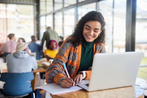 istock Young female college student smiling while doing homework in a school cafeteria 1874699761