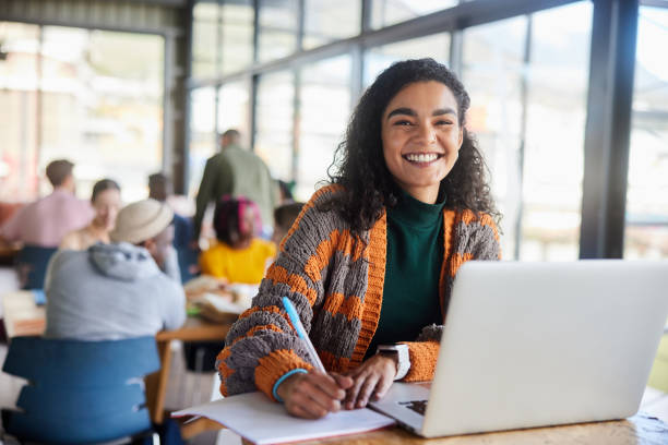 istock Smiling female college student doing homework at a cafeteria table at school 1874700387