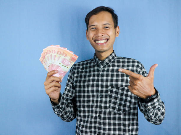 istock Excited expression handsome asian man hold paper money banknotes with pointing aside gesture 1874701445