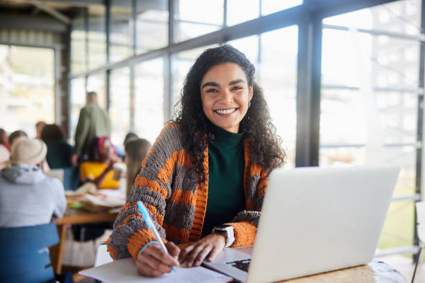 istock Young female college student smiling while doing homework in a campus cafeteria 1874703519