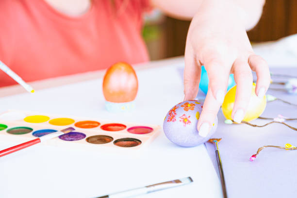 Woman hand painting easter egg with watercolors, preparation for egg hunt game. Happy easter congratulation symbol.