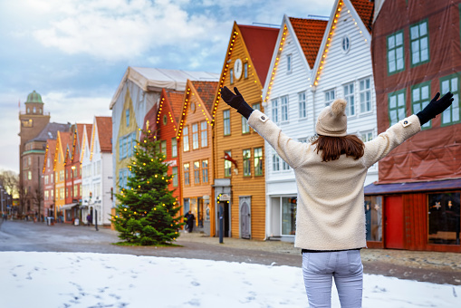 A happy tourist woman looks at the Christmas deocrated Bryggen district in Bergen, Norway, during a winter day with snow