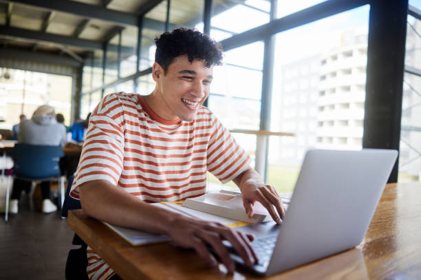 istock Young male college student laughing while working on a laptop in a cafeteria 1874712304